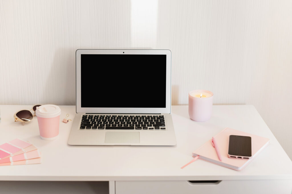 open laptop on white desk with pink office accessories